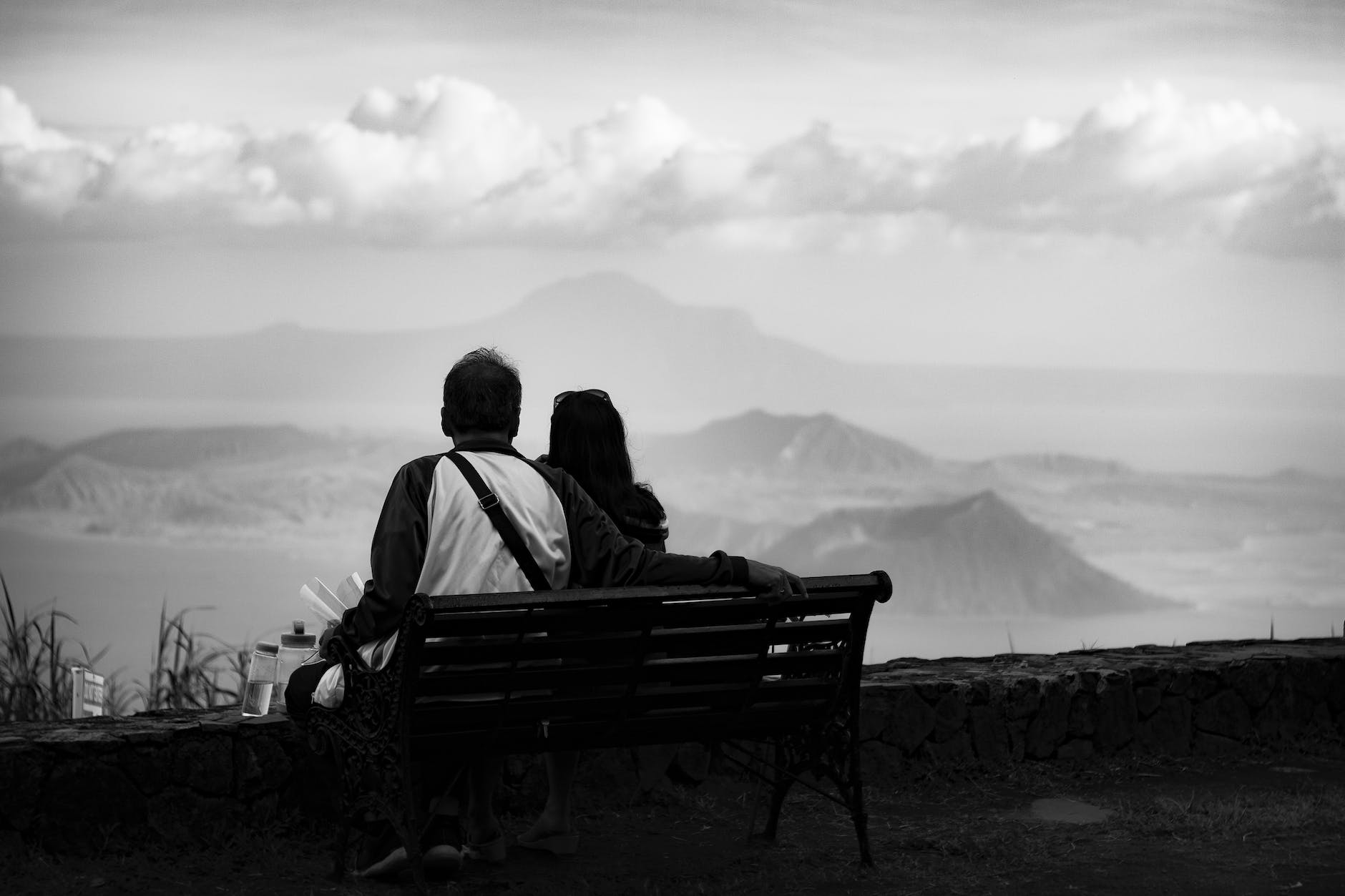 anonymous travelling couple resting on bench and enjoying mountain view