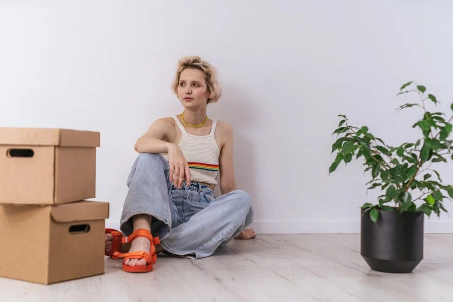 Woman with cardboard boxes and a plant in a white room